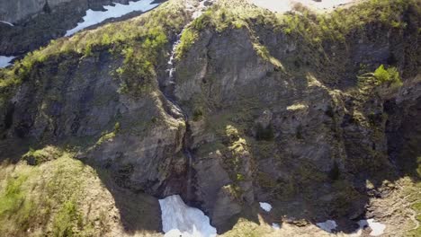 Zoom-out-of-a-waterfall-in-the-Swiss-Alps,-with-some-snow-around