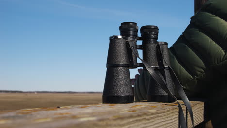 Person-sets-binoculars-on-watch-tower-rail-and-looks-out