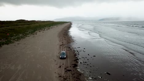 Drohnenansicht-Eines-Autos,-Das-An-Einem-Riesigen-Irischen-Strand-Fährt