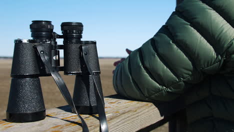 Person-sets-binoculars-on-wooden-guard-rail