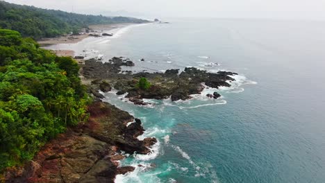 Aerial-View-Flying-Above-Rocky-Pacific-Coast-Jungle-Beach-With-Blue-Water-Waves-Crashing-Onto-Shore-In-South-America