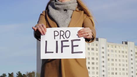 Attractive-woman-holding-paper-with-PRO-LIFE-words-with-cityscape-in-background