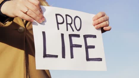 Female-holding-PRO-LIFE-board-against-blue-sky,-close-up-view