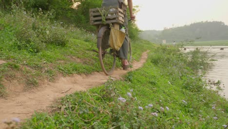 Low-angle-shot-of-farmer-on-a-cycle-on-a-graval-pathway-along-the-river-bank-in-Loc-Binh-along-rural-district-Lạng-Sơn-province-in-the-Northeast-region-of-Vietnam