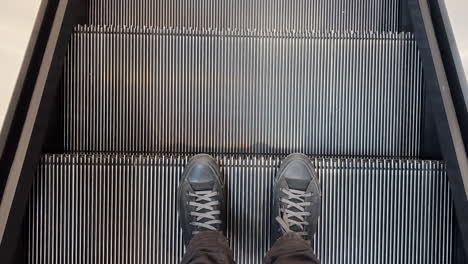 Male-feet-in-black-sneakers-on-escalator-in-shopping-mall,-top-view-pov