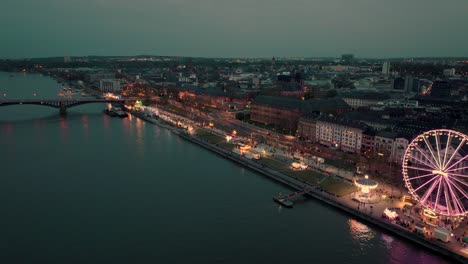 Drone-aerial-shot-of-Mainz-pulling-back-from-a-wine-festival-showing-the-whole-city-in-a-wide-shot-over-the-Rhine-river-at-a-summer-sunset-with-lots-of-city-lights