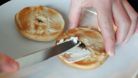 Spreading-cream-cheese-on-to-a-bagel-with-a-knife