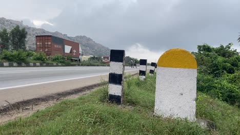 Captured-Real-Photo-of-Plain-Yellow-and-White-Milestone-with-National-Highway-Road-and-green-plants-Background-which-can-be-used-for-writing-Kilometre-numbers
