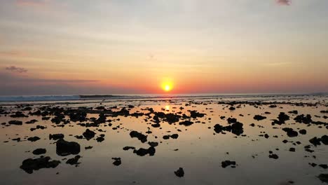 Dramatic-drone-shot-of-the-coast-at-low-tide-at-Gili-Trawangan,-Bali,-Indonesia-and-sunset-behind-the-pier