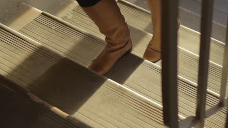 High-angle-closeup-of-woman-boots-shoes-going-up-stairs,-golden-hour-sunlight