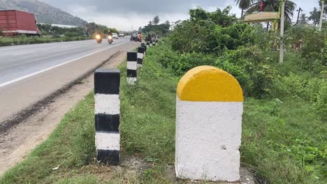 Plain-Yellow-and-white-milestone-with-national-highway-road-with-traffic-flow-and-green-plants-background