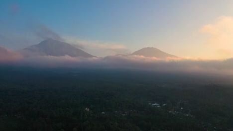 Dramatic-aerial-view-of-2-volcanoes-of-a-beautiful-mountain-range-surrounded-by-clouds-during-sunrise-on-the-background