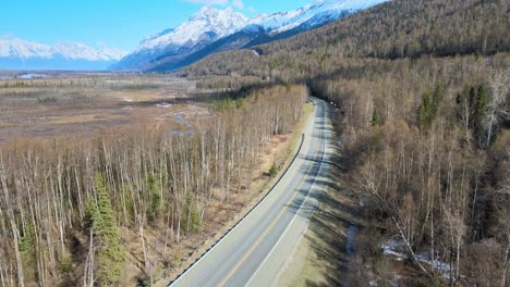 Aerial-view-of-country-road-with-mountains-on-the-right-and-swamp-on-the-left-in-the-spring-prior-to-the-foliage-turning-green