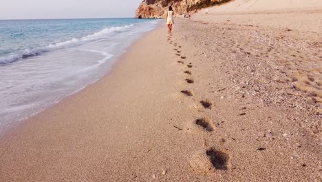 Mujer-Deja-Huellas-Durante-La-Caminata-En-La-Playa-De-Milos,-Isla-De-Lefkada,-Grecia---Revelación-Aérea
