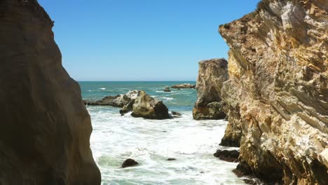 The-sea-rushes-in-between-two-cliffs-along-a-rocky-coast-in-Southern-California---pull-back-slow-motion