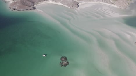 Boat-Cruising-Through-Shallow-Waters-Near-An-Island---aerial-shot