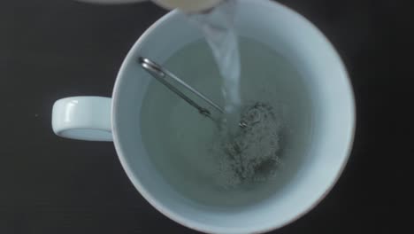 Pouring-hot-water-on-tea-strainer-with-herbs-in-mug,-top-down-view