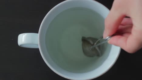 Mixing-tea-stainer-with-tea-herbs-in-mug-with-hot-water,-top-down-view