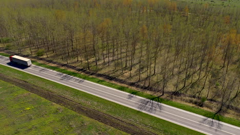 Semi-truck-driving-on-the-road-through-wooded-landscape,-drone-point-of-view