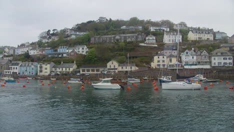 Looe-Hillside-Waterfront-Homes-Overlook-Sailboats-Moored-in-Harbour,-South-Coast-Cornwall,-United-Kingdom,-Wide-Shot