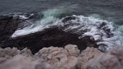 Evening-waves-from-atlantic-ocean-washing-up-on-rocky-shoreline-at-evening--High-angle-with-cliff-close-to-camera-and-looking-down-at-waves---Static-clip-from-Sotra-island-outside-Bergen-Norway