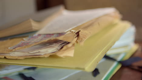 A-man's-hand-places-a-yellow-folder-and-an-old-torn-envelope-on-a-disorganized-pile-of-folders