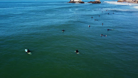 Vista-Aérea-De-Los-Surfistas-Acostados-En-La-Tabla-De-Surf-Esperando-Olas-Para-Surfear
