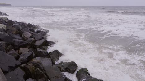 Slow-motion-view-of-sea-crashing-onto-rocks-on-a-dull-day,-Whitby-North-Yorkshire-England-UK