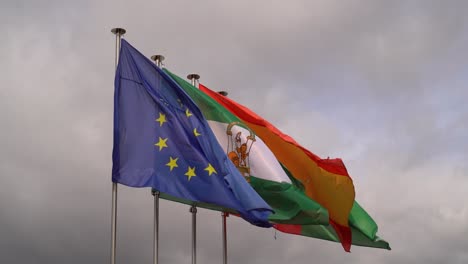 European-flag-in-front-of-Spanish-and-Andalusian-flag-waving-against-gray-sky
