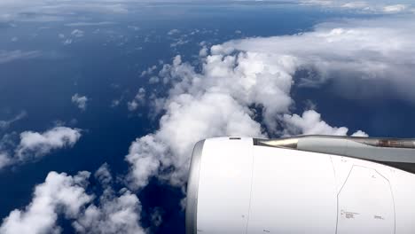 Looking-out-the-window-of-a-commercial-airplane-on-a-flight-over-a-blue-ocean-with-a-jet-engine-in-frame