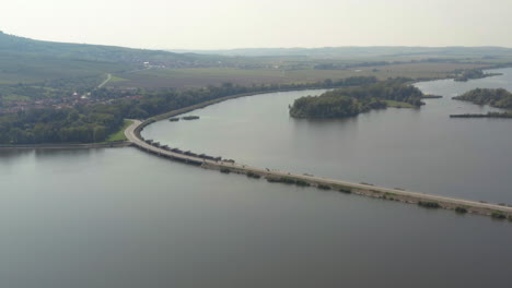 Motorbikes-driving-fast-on-Věstonice-reservoir-causeway,-drone-shot