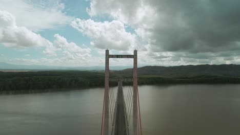 Drone-flying-forwards-through-the-hollow-of-a-long-gray-bridge-spanning-a-large-South-American-river