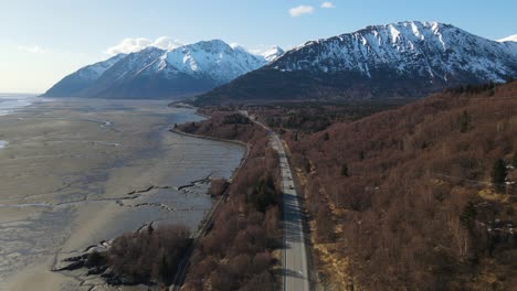 4K-drone-flying-along-the-coast-of-Alaska-showcasing-trees-snow-and-mountains-in-the-evening-early-spring