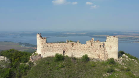 Ruins-of-Děvičky-castle-in-Moravia,-Mikulov-in-distance,-drone-shot