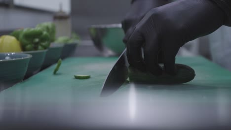 Chef-cutting-a-cucumber-using-a-knife-with-black-gloves-on-a-green-cutting-board