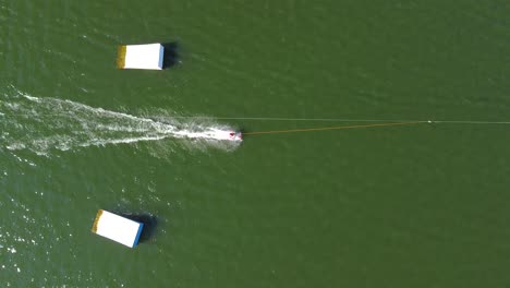 Birds-eye-view-drone-shot-of-a-waterski-system---drone-is-ascending-over-some-ramps-with-waterskiers-and-wakeboarders-passing-by