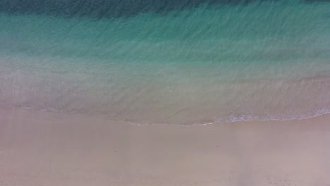Static-aerial-top-down-shot-of-blue-turquoise-sea-shore-water-while-waves-break-quietly