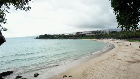 Playa-De-Mauna-Kea-En-La-Isla-Grande-De-Hawaii-Con-Vista-Al-Océano-Y-Un-Hotel-Resort-En-La-Distancia---Toma-De-Grúa-Ascendente-Enmarcada-Por-árboles