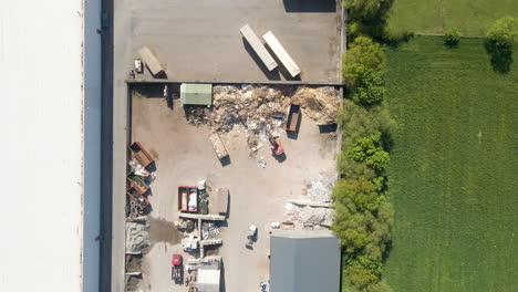 Top-down-aerial-of-excavator-sorting-metal-at-recycling-center---drone-slowly-setting-down