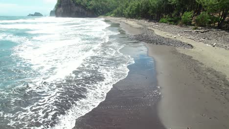 Waves-crashing-against-black-sand-beach-shore-on-Wilderness-Location,-Aerial-downward-tilt-up