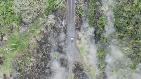 Car-driving-in-narrowed-lonely-isolated-road-in-tropical-hawaii-island-with-lava-smoke-from-the-volcano