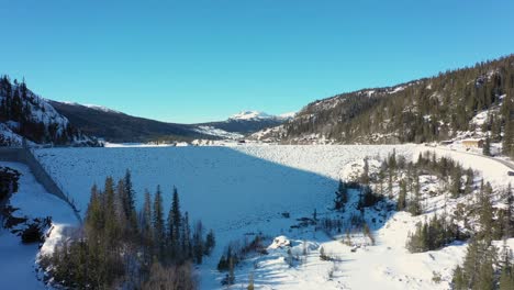 Represa-Tunhovd-Y-Revista-De-Agua---Presa-Aérea-Que-Se-Acerca-A-La-Presa-Cubierta-De-Nieve-De-Lejos-A-Cerca-Con-Montañas-Y-Cielo-Azul-Fondo-Natural---Presa-Statkraft-Para-La-Central-Hidroeléctrica-Nore-Noruega