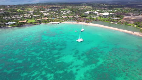 Sailboats-anchored-in-the-turquoise-bay-near-Anaehoomalu-on-the-Big-Island-of-Hawaii-and-nearby-hotels---ascending-aerial-view