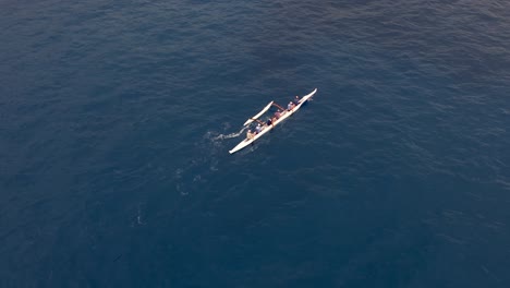 A-rowing-team-paddles-a-Hawaiian-outrigger-canoe-along-the-ocean-in-synchrony---aerial-bird's-eye-view