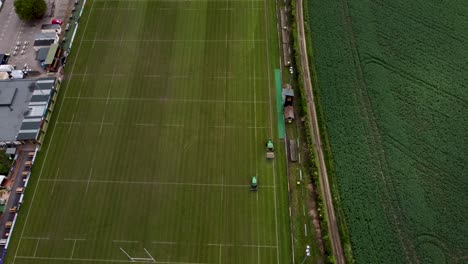 Langsame-Luftaufnahme-Von-Zwei-Traktoren,-Die-Das-Gras-Auf-Dem-Canterbury-Rugby-platz-In-Kent-Schneiden