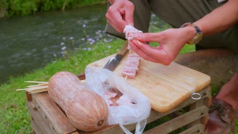 Close-up-of-a-person-assembling-meat-skewers-for-a-barbecue-picnic-by-a-river