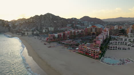 Tiro-De-Drone-Del-Hotel-Resort-En-Playa-El-Médano-Con-Montañas-En-La-Distancia-En-Cabo-San-Lucas-Mexico,-Ancho-Y-Giratorio