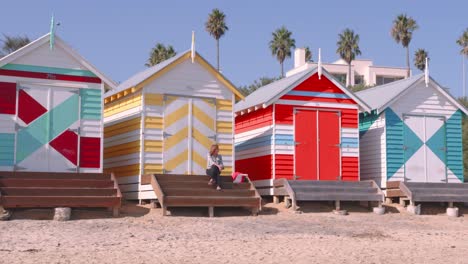 A-lady-sitting-on-the-steps-of-one-of-the-iconic-brightly-painted-beach-hut-on-Brighton-Beach-Victoria