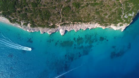 Bird-eye-view-drone-shot-of-Albanian-coast-in-the-Mediterranean-sea---drone-is-descending,-watching-a-speed-boat