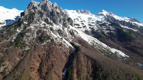 Flying-toward-epic-mountain-peak-covered-in-white-snow,-beautiful-Albanian-Alps